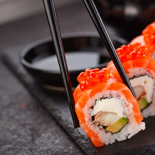 Chopsticks picking up a uramaki with salmon, cream cheese, and ikura.