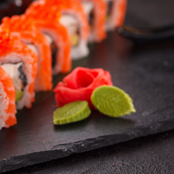 Chopsticks picking up a uramaki with salmon, cream cheese, and ikura.